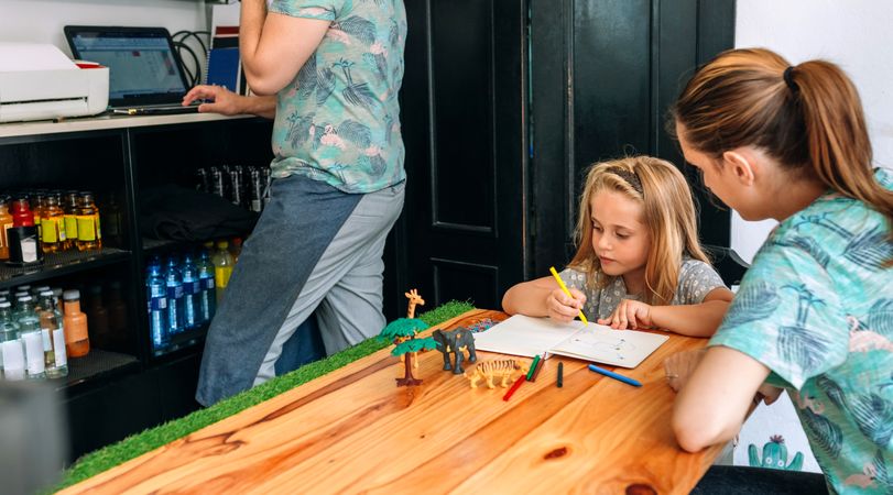 Mother drawing with her daughter while father works in their own coffee shop