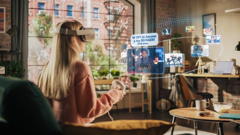 Woman Sitting in Loft Living Room at Home, Using Virtual Reality Headset with Controllers to Check Social Media Streaming App