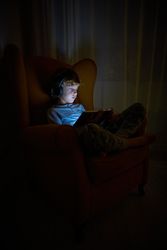 Boy in headphones playing on tablet in darkness