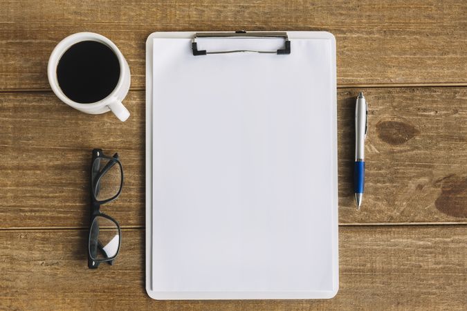 Tea, pen, and spectacles next to blank papers with clipboard on wooden table