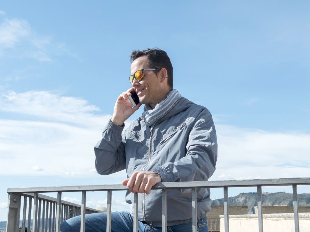 Happy smiling man talking on the mobile phone while standing outside