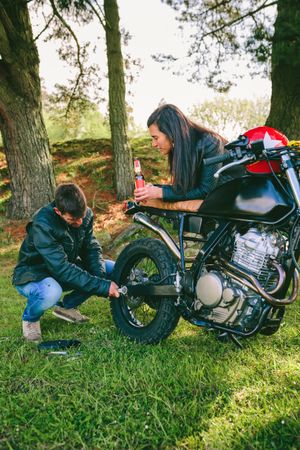 Man fixing his motorcycle while his girlfriend looks at him