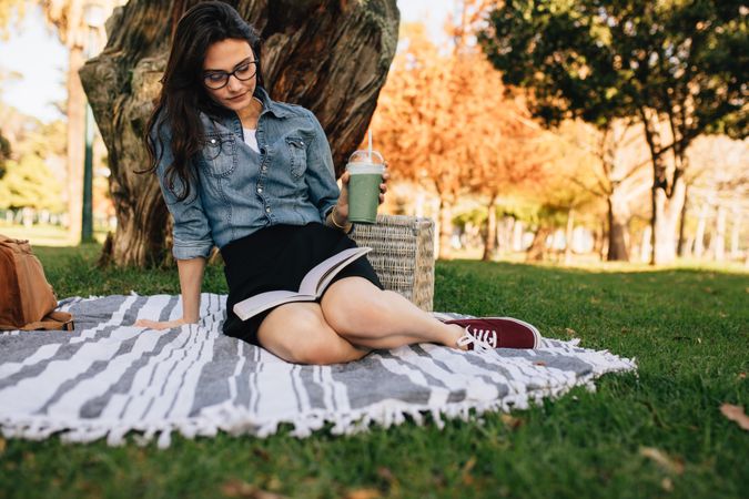 Young woman reading a book sitting on a blanket at the park