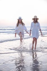 Smiling girlfriends in summer clothes barefoot in water on beach