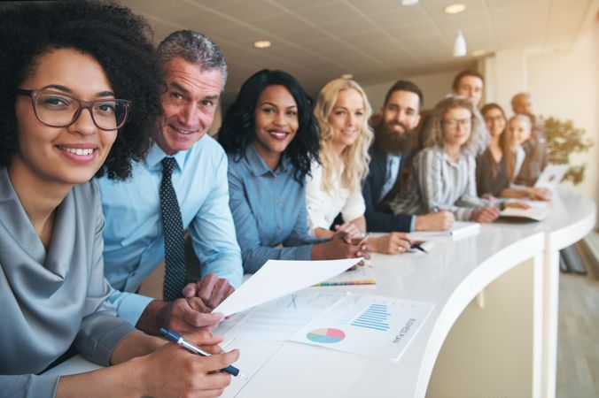 Multi-ethnic group of people in office attire smiling in a row at work
