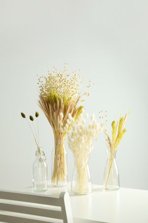Four glass vases with dried flowers in grey room, vertical composition