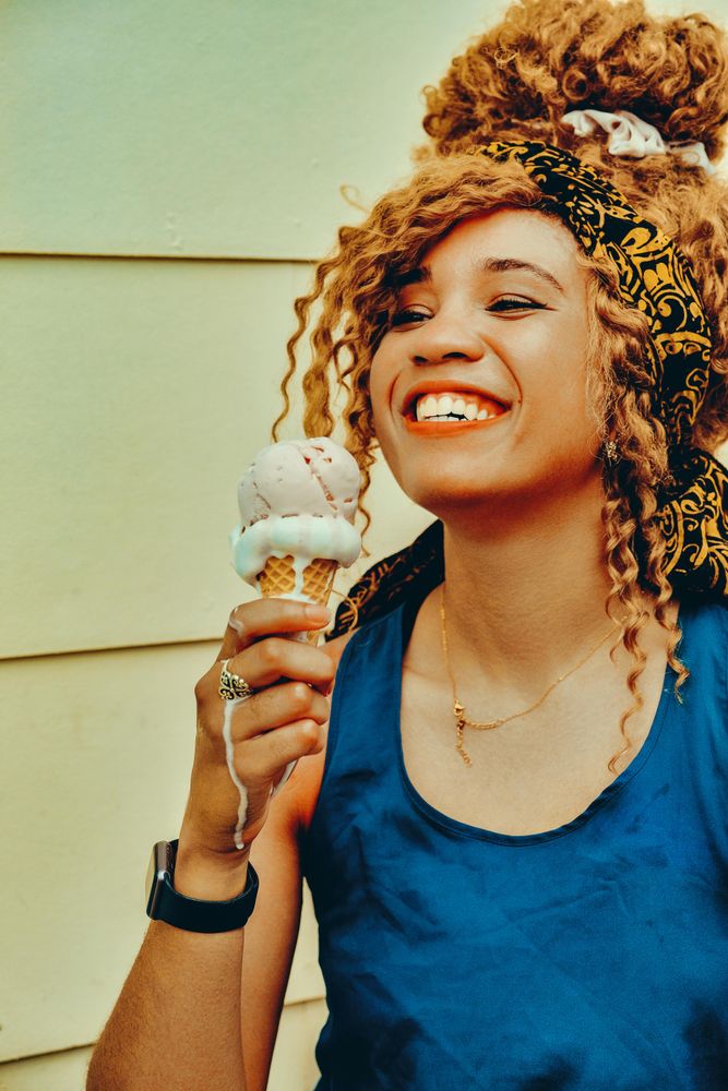 Vertical shot of smiling Black female enjoying an ice cream cone in the sun, copy space