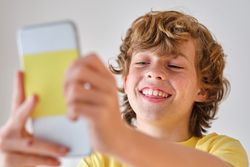 Content boy taking selfie on smartphone on light background