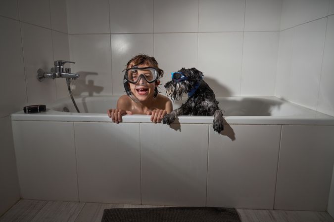 Cheerful boy in diving mask near dog in tub