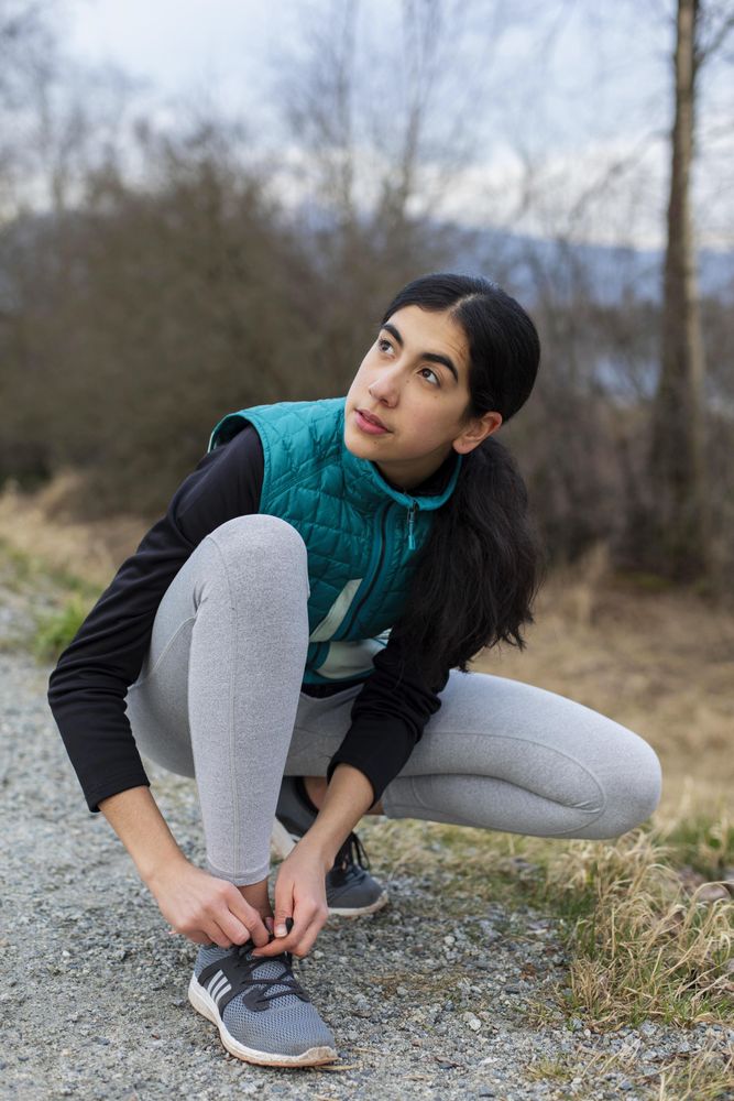 Young woman looking away while tying her shoe laces