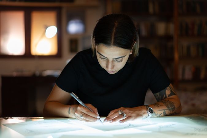 Tattooed woman illustrating on tracing paper on a light table
