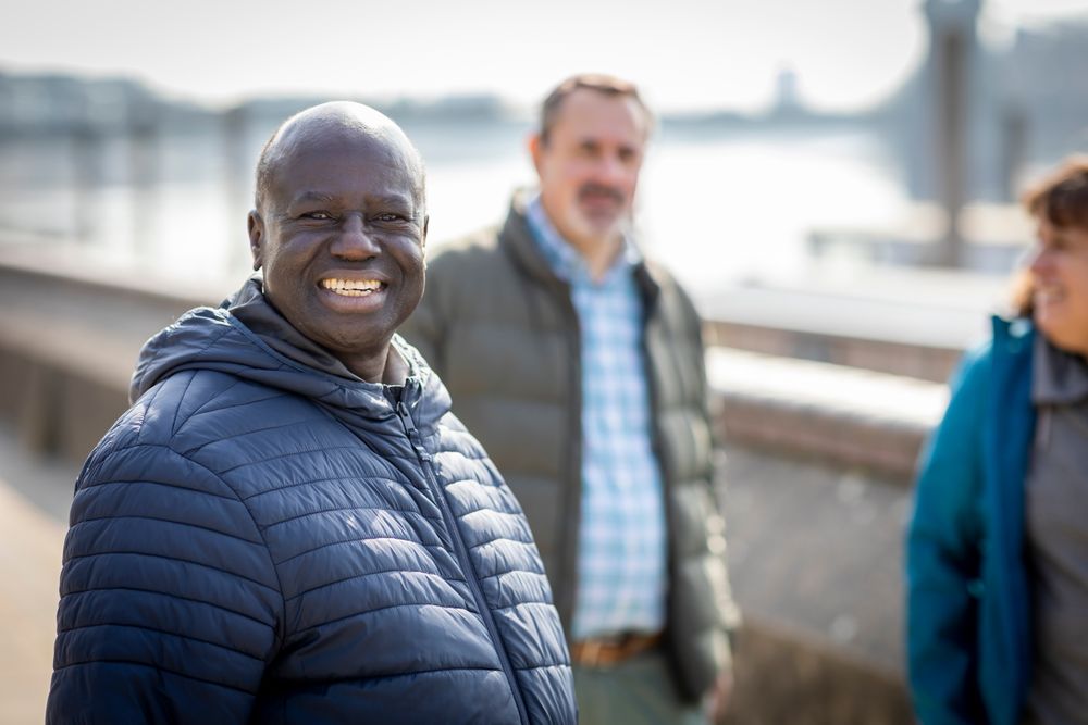 Smiling Black man walking by the river with people behind him