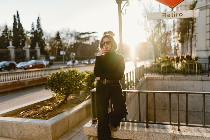 Stylish woman lighting cigarette near metro station