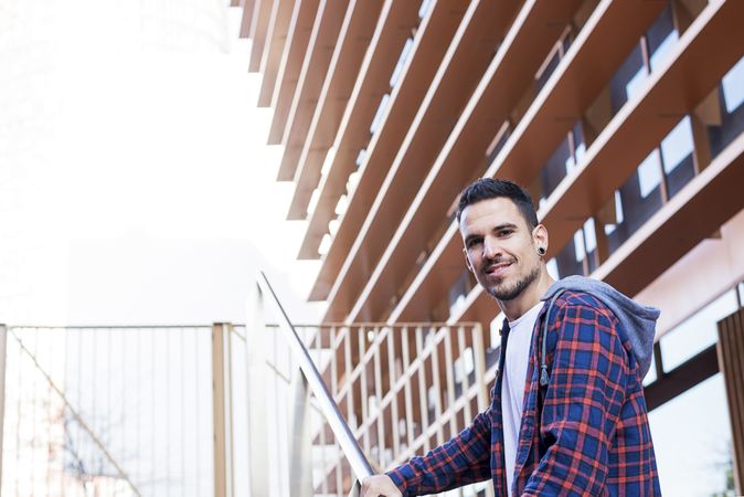 Smiling man in plaid shirt walking up stairs on a sunny day with copy space