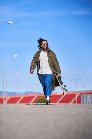 Stylish man walking with longboard on stadium