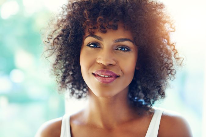 Portrait of female with curly hair half smiling on blurry leafy background
