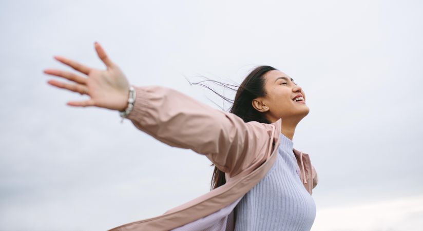 Blissful young woman stretching arms out in wind
