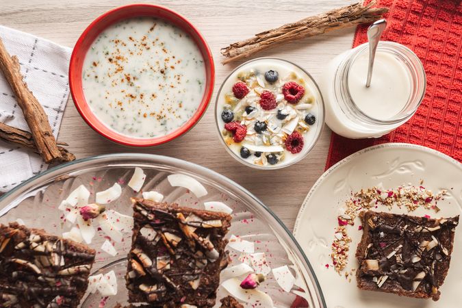 Yogurt in glass bowl with berries and cinnamon sticks and sliced brown cake