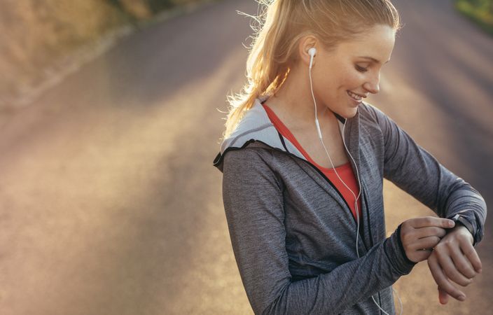 Woman athlete looking at her watch standing on road