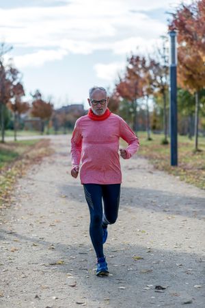 Grey haired man in red shirt jogging outside in park