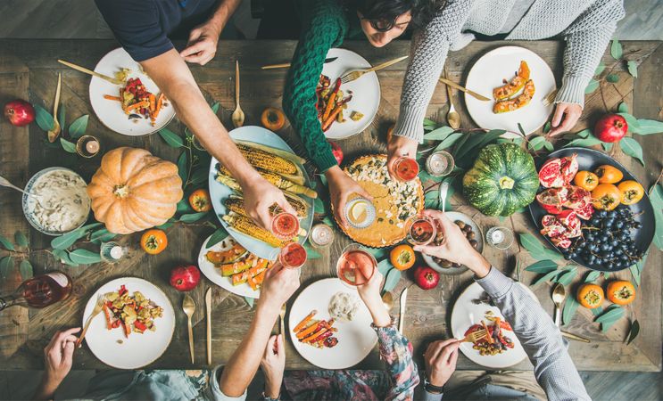 Group of people toasting with wine at festive vegetarian table setting with pie and corn
