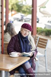Woman reading book while sitting at an outdoor table at a coffee shop. 4mDvX5