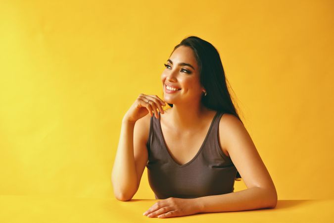 Smiling Hispanic woman looking wistfully away from camera and sitting in yellow room, copy space