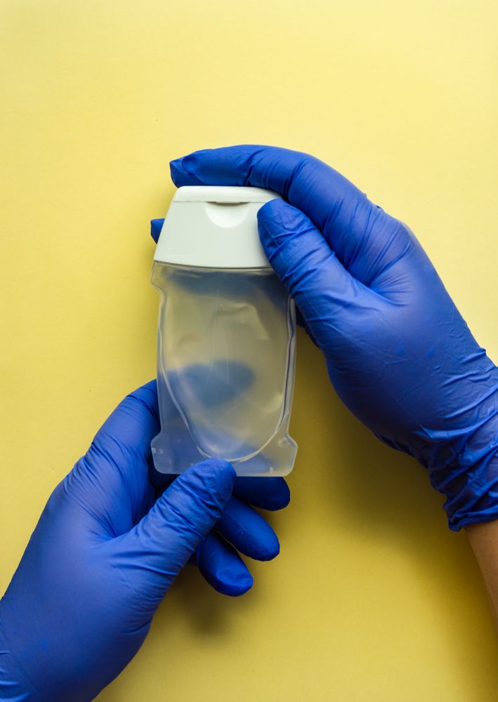 Top view of yellow table with hands wearing protective blue gloves holding soap