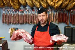 Man holding chunks of ham behind counter in butcher shop 43R2g5