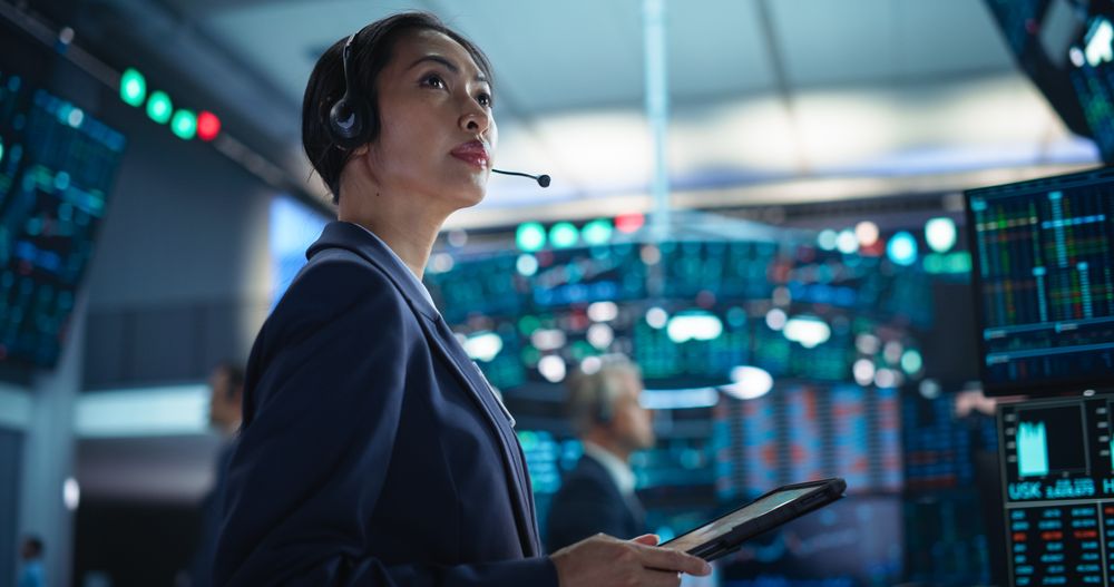 Young Asian Female Broker Working on Tablet Computer on Stock Exchange Floor.