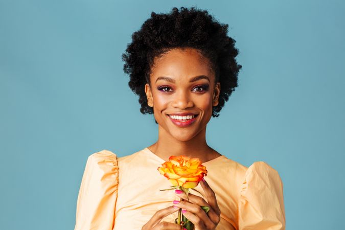 Studio shot of a smiling Black woman holding a yellow rose