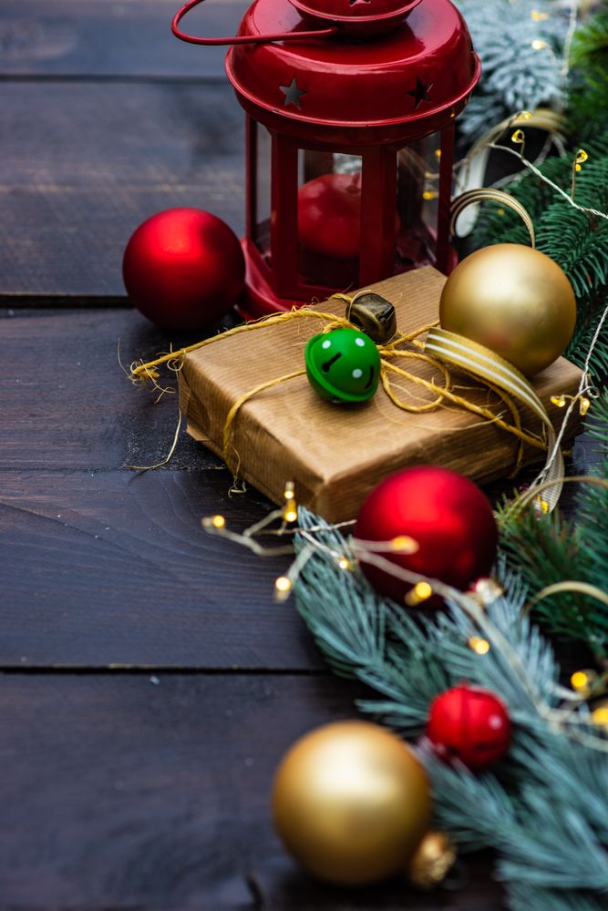 Close up of Christmas gift wrapped in brown paper surrounded by baubles, fir and lights