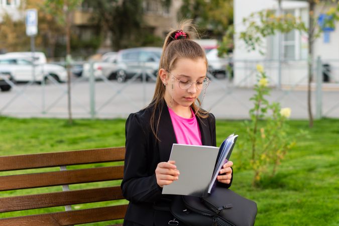 Girl reading book, seated on bench