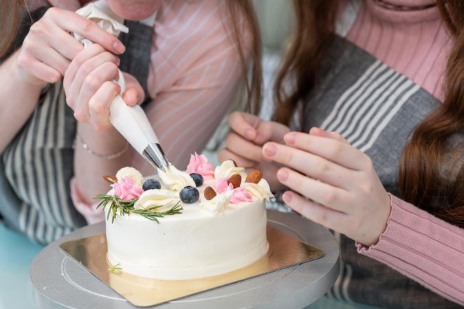 Two women decorating a cake with frosting