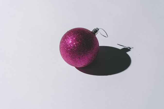 Pink Christmas ornament with pastel grey background and deep shadows