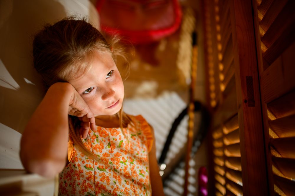 Bored girl leaning on hand against shutters in sunbeams