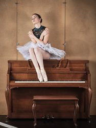 Graceful ballerina in tutu and pointe shoes sitting on piano