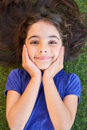 Girl lying on grass and touching cheeks