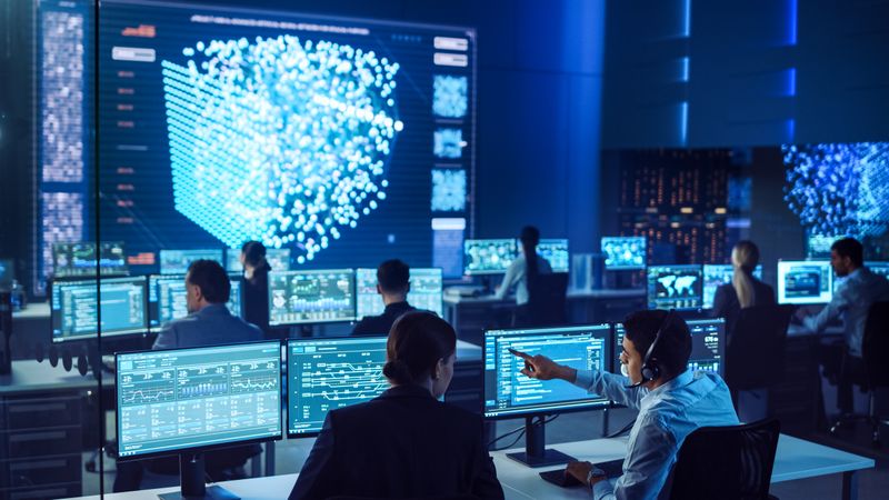Diverse Professionals Collaborate in a High-tech Control Room, Analyzing Data on Multiple Screens to Enhance Cybersecurity and Operational Strategies. the Environment Fosters Innovation and Strategic Decision-making.