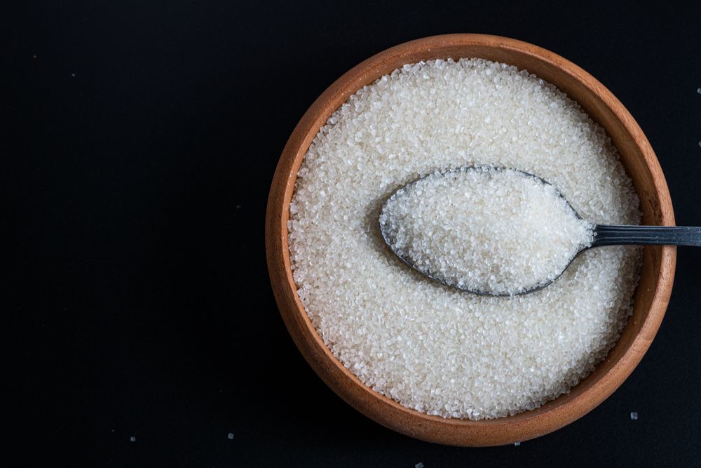 Flat lay of a wooden bowl filled with sugar and a stainless spoon resting on top