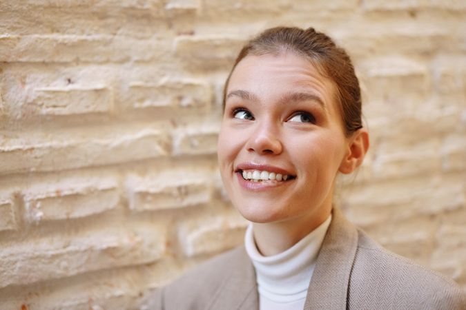 A cheerful and youthful young woman is smiling brightly against a beautifully textured wall