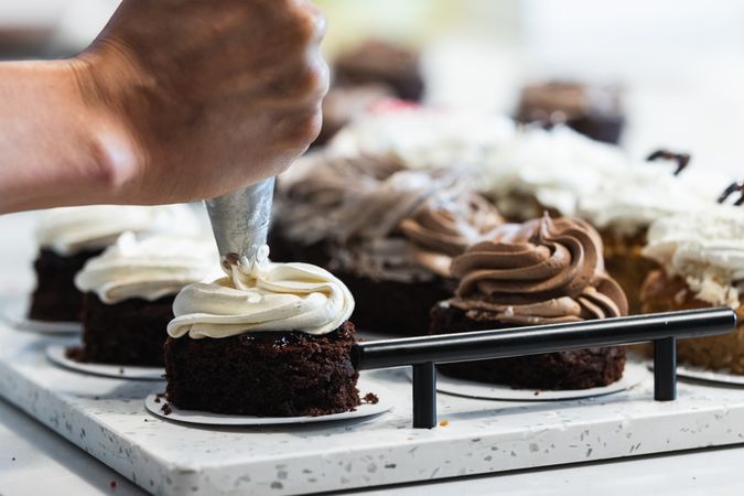 Crop cook adding whipped cream on sponge cakes in bakery