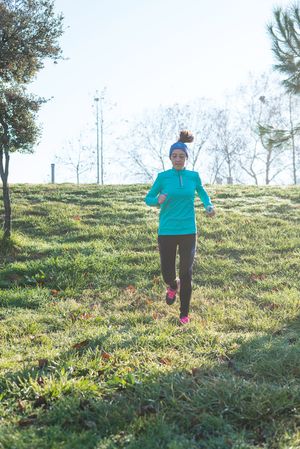 Woman in blue jogging in grass on sunny fall day