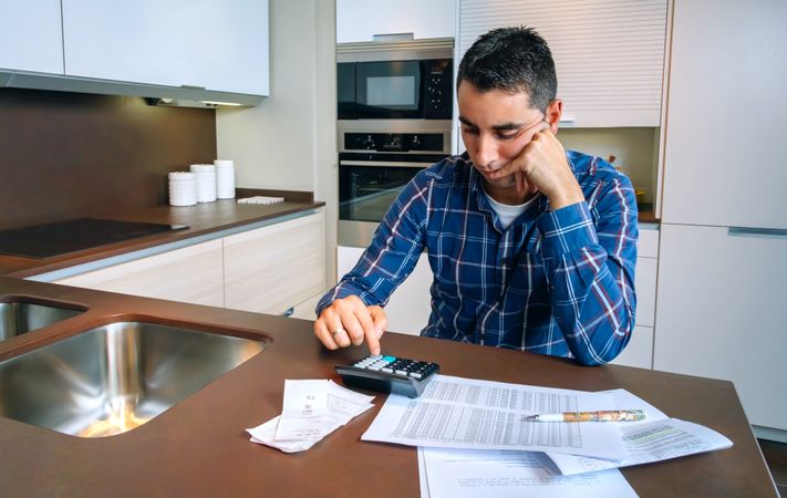 Man with calculator and bills in kitchen