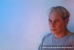 Portrait of sad middle aged man in gray shirt against light background in UV lit studio 5pKmg0