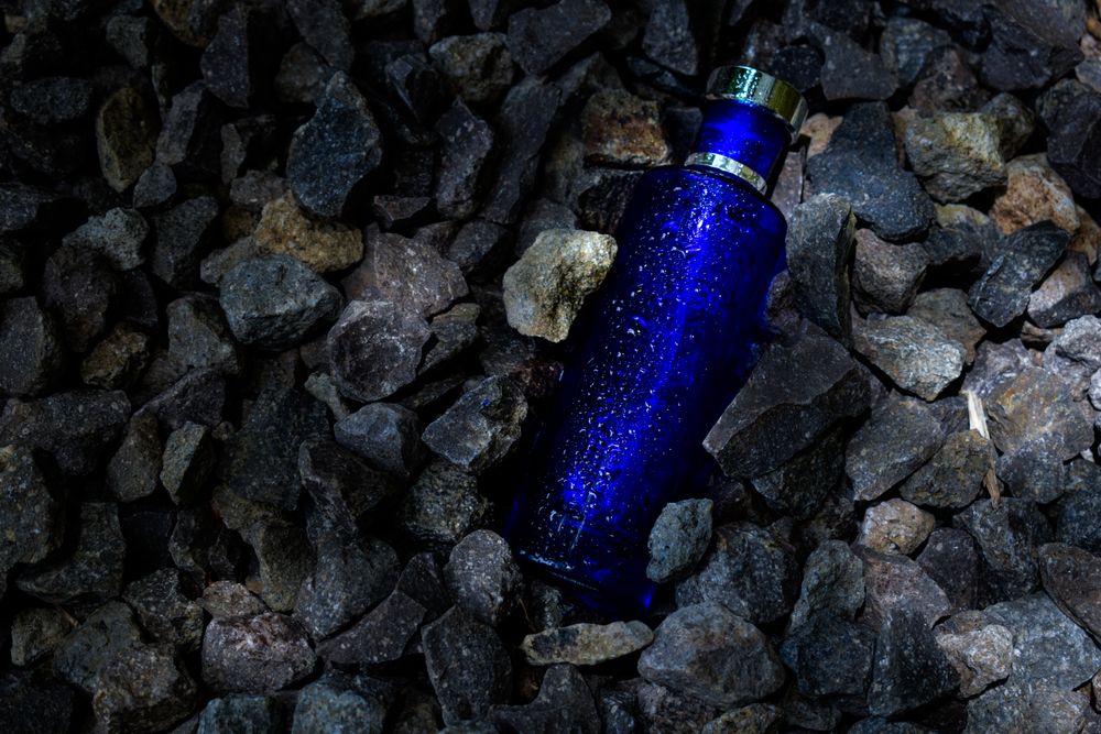 Blue perfume bottle mock up laying in rocky terrain