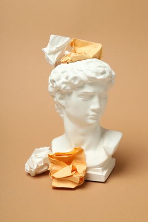 Marble bust with crumpled paper on brown background, vertical
