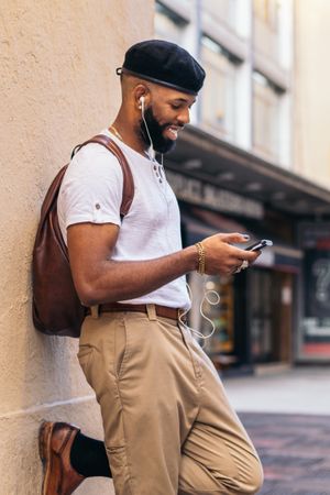 Stylish Black man using smartphone and listening to music outdoors in the city
