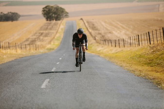 Athlete cycling on empty road in countryside