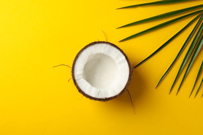 Half of coconut and palm leaf on yellow background, top view